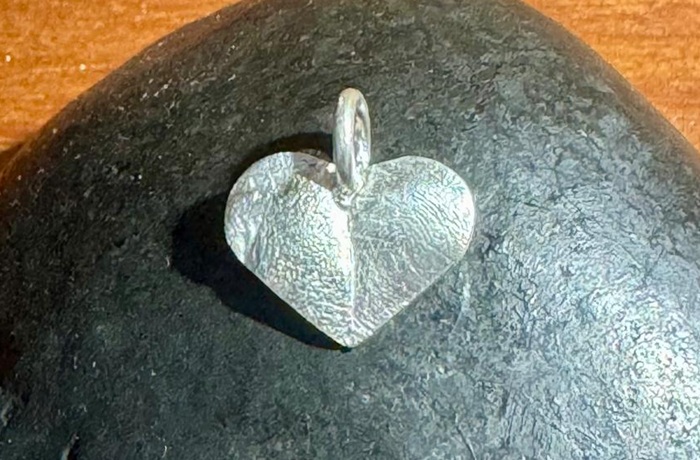 Heart-shaped nose and paw-print pendant resting on a smooth stone